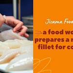 a food worker prepares a raw fish fillet for cooking